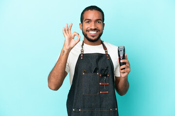 Wall Mural - Young hairdresser latin man isolated on blue background showing ok sign with fingers