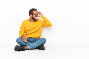 Wall Mural - Young Ecuadorian man sitting on the floor isolated on white wall laughing