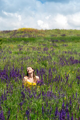 An adult girl in an orange dress is sitting and smiling among the sage in a meadow. Communication with nature. Selective focus.