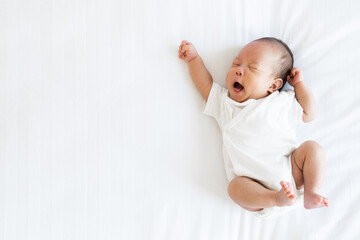 portrait of asian newborn baby in white cloth on bed funny pos