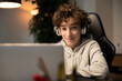 © ABCreative - A young boy with curly hair is happy with remote learning. A student sits in front of a computer with wireless headphones listening to a teacher lecture. The lessons take place over the Internet.