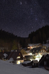 Wall Mural - Starry night sky above a small mountain village with snow. Village Petrikov in Jeseniky mountains.