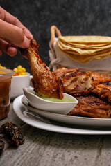 Canvas Print - A vertical shot of a roasted chicken thigh dunk in a green sauce, and thin flatbread in the background