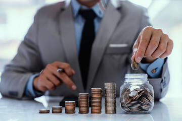 Wall Mural - Asian businessman holding coins in a piggy bank to collect money About Finance Accounting Income Tax and Accounting while the concept of maximizing profit from business investments, saving money