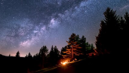 Wall Mural - bunch of friends sitting over campfire in summer nature forest under magic milky way galaxy stars as