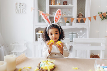 Wall Mural - Little African American girl paints Easter eggs at home in the kitchen. happy easter.