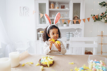 Wall Mural - Little African American girl paints Easter eggs at home in the kitchen. happy easter.