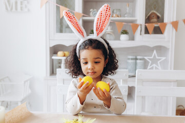 Wall Mural - Little African American girl paints Easter eggs at home in the kitchen. happy easter.