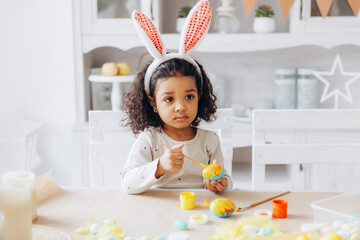 Wall Mural - Little African American girl paints Easter eggs at home in the kitchen. happy easter.