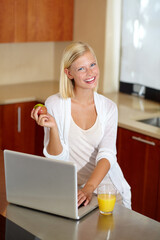 Wall Mural - Checking up on her schedule for the day. A lovely young woman using her laptop while enjoying a healthy breakfast.