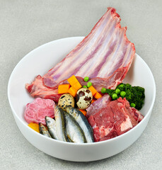 Wall Mural - Natural raw dog food. Fresh raw meat, fish and vegetables in bowl on grey background.