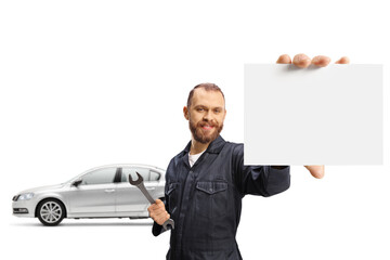 Wall Mural - Mechanic posing in front of a car and holding a wrench and a small blank card