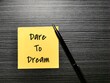 Phrase dare to dream written on sticky note with a pen.