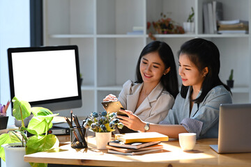 Wall Mural - Two young female office workers sharing idea and working on project together.