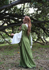 Canvas Print - Full length portrait of blondewoman wearing a  beautiful  green medieval fantasy gown. Posing with gestural hands in a enchanted forest background.