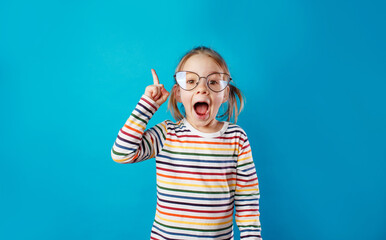 a little girl in big glasses and a striped T-shirt stands on a blue isolated background with her mouth wide open.