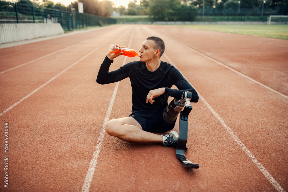 A thirsty sportsman with artificial leg sitting at stadium drinking refreshment.