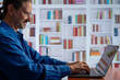 Smiling mature man working on laptop in library setting with bookshelves, remote work.