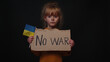 © Andrii Iemelianenko - Upset Ukrainian poor toddler girl kid homeless protesting war conflict raises banner with inscription massage text No War on black background. Crisis, peace, stop aggression, child against Russian war
