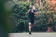 Determined young man running outside in the park. Fit boy doing exercise outdoor. Beautiful sporty male run alone. Sweaty athlete training with towel. Wellness, health, sport, fitness open air concept