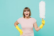 © ViDi Studio - Elderly excited fun housewife woman 50s in pink t-shirt gloves doing housework hold white duster brush isolated on plain pastel light blue background studio. Housekeeping cleaning tidying up concept.