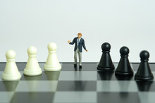 Miniature People Toy Figure Photography. Strategy Decision Concept. A Shrugging Unsure Businessman Stand Above Chessboard With Black White Chess Pawn. Isolated On White Background