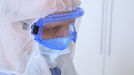 Close-up of a tired face of a doctor in goggles, a mask and a sterile gown. Sterile clothing in the infectious disease department with patients with coronovirus