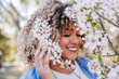 © Eva - portrait of happy hispanic woman in spring among pink blossom flowers. selective focus on flowers