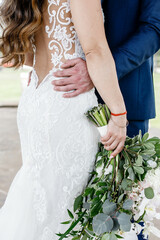 Wall Mural - Young loving wedding couple hugging Portrait of a bride in white gown and groom in blue suit Bride is holding white wedding bouquet with greenery Close up 