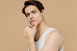 © ViDi Studio - Attractive handsome calm young man 20s perfect skin in undershirt look camera prop up chin isolated on pastel pastel beige background studio portrait. Skin care healthcare cosmetic procedures concept.