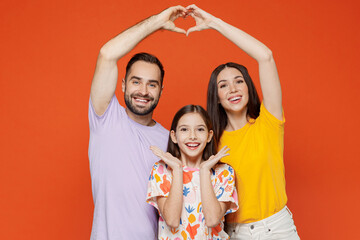 Wall Mural - Young parents mom dad with child kid daughter teen girl in basic t-shirts hold hands above head showing shape heart with hands heart-shape sign isolated on yellow background studio Family day concept