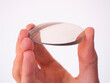 Hand holds a circular lens of cut glass, lens cut for eyewear, production of clear lens for eyewear.