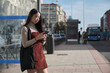 © Ladanifer - Young asian woman checking her smartphone while waiting for the bus at bus stop.