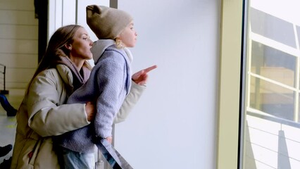 Wall Mural - Young woman and her daughter stand look a plane from the while waiting a boarding at the airport