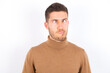 © Roquillo - young caucasian man wearing grey turtleneck over white background making grimace and crazy face, screaming out of control, funny lunatic expressing freedom and wild.