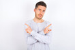© Roquillo - young caucasian man wearing grey sweater over white background crosses arms and points at different sides hesitates between two items or variants. Needs help with decision