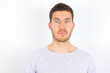 © Roquillo - Stunned young caucasian man wearing grey sweater over white background stares reacts on shocking news. Astonished young man holds breath
