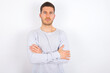 © Roquillo - Confident young caucasian man wearing grey sweater over white background with arms crossed looking to the camera