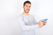 © Roquillo - Nice addicted cheerful young caucasian man wearing grey sweater over white background using gadget playing network game