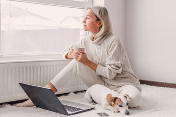 Wall Mural - Happy middle aged woman with dog using her laptop at cozy white home