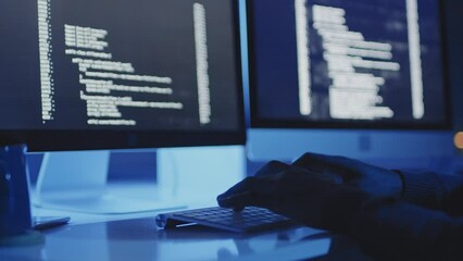 Low angle of hands of cropped male programmer sitting at desk in dark modern office, typing on keyboard, coding on computer