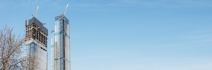 Construction of modern high-rise buildings. Two skyscrapers under construction against the blue sky. Banner format.