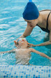 © ninelutsk - Toddler child learning to swim in indoor swimming pool with teacher. Floating in the water, balancing and general physical activity for kids, early development. Boy kid trained to kick legs and float