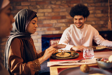 Wall Mural - Young Middle Eastern woman eats with her family at dining table at home.