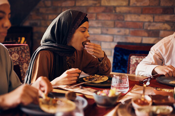 Wall Mural - Young Muslim woman enjoys while eating falafel while eating with family at home.