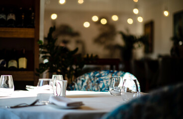 Poster - Glasses, flower fork, knife served for dinner in restaurant with cozy interior.