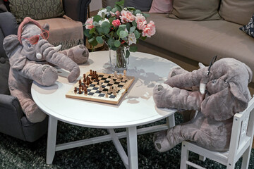 Two plush elephants in glasses play chess at a white table.