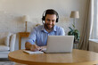 © fizkes - Man in headset sit at desk make notes in copybook, writes helpful information while negotiates, studying remotely via video call app on laptop. Improve skills, educational webinar use internet concept