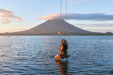back view of woman sitting on a swing overlooking the volcano concenpcion on ometepe island, nicarag