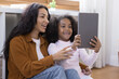 © fizkes - Happy two female generations African American family using digital touchpad gadget, holding web camera call conversation, watching funny video online, choosing goods shopping in internet store.